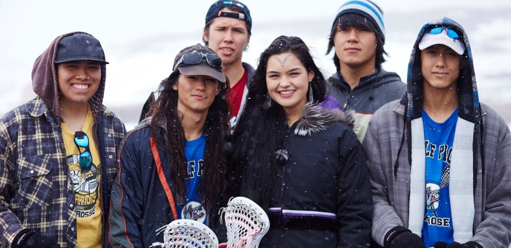 A group of young Indigenous people, smiling and posing together in the snow, showcasing a sense of community and joy, while dressed in casual winter clothing.